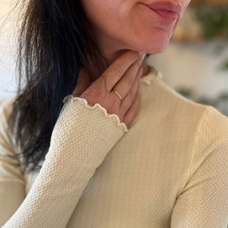Close-up of a person wearing a  9 ct gold ring and a beige long-sleeve top with scalloped trim.