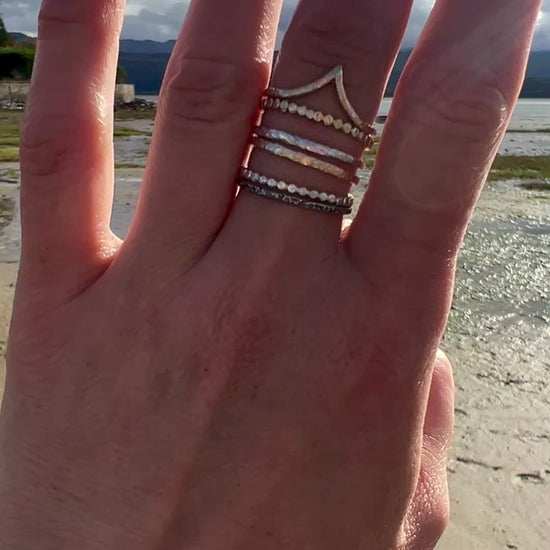 Stacking rings in gold silver worn on a hand, there is a beach in the background. lifestyle video from a walk presenting rings worn as an everyday piece of adornment
