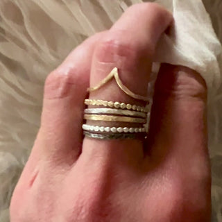 A video of a female hand touching a soft fabric. There is a set of 9ct gold and textured silver stacking rings on the middle finger. The rings belong to Six elements goddess collection.