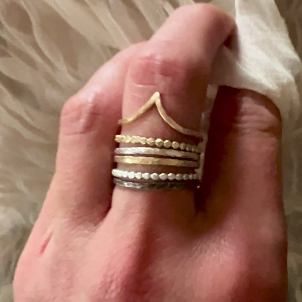 A video of a female hand touching a soft fabric. There is a set of 9ct gold and textured silver stacking rings on the middle finger. The rings belong to Six elements goddess collection.