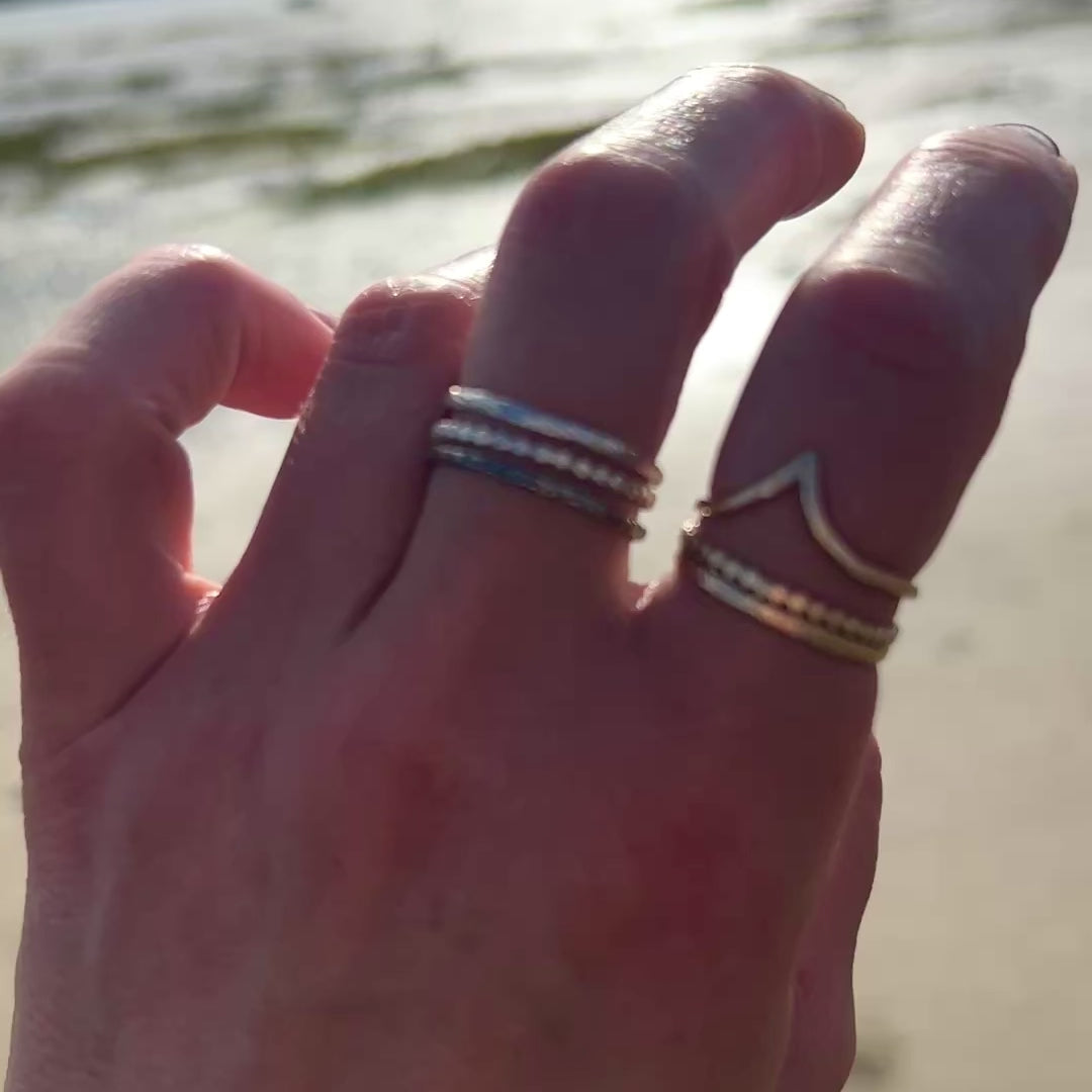 two stacks of stacking rings silver trinity and golden trinity worn on a hand there is a beach in the background.